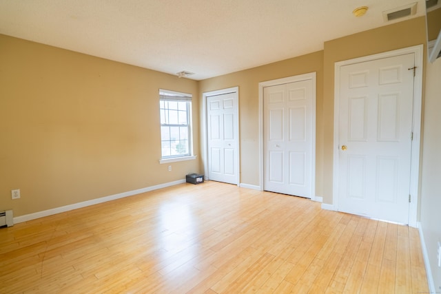 unfurnished bedroom with wood finished floors, visible vents, two closets, and baseboards