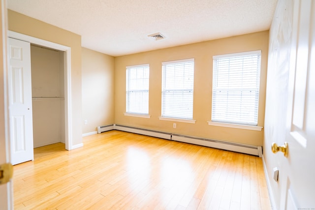 unfurnished bedroom with baseboards, light wood finished floors, visible vents, a textured ceiling, and baseboard heating