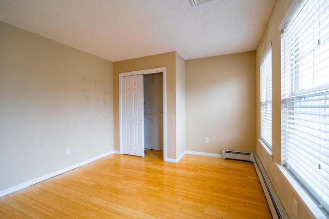 empty room featuring light wood-type flooring, baseboards, a textured ceiling, and baseboard heating