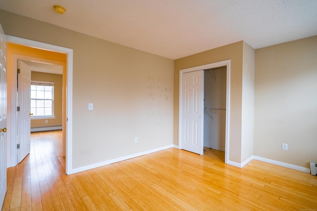 unfurnished bedroom featuring a baseboard heating unit, a closet, baseboards, and light wood finished floors