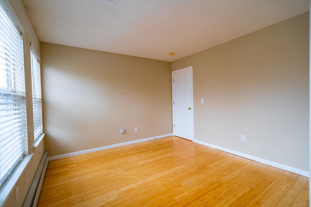 spare room with a textured ceiling, baseboards, light wood finished floors, and a baseboard radiator