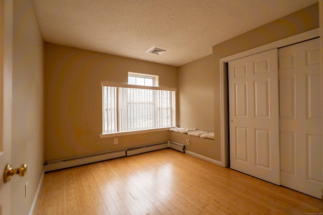 unfurnished bedroom with a textured ceiling, wood finished floors, visible vents, and a baseboard radiator