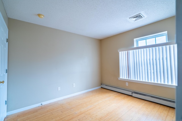 empty room with a textured ceiling, wood finished floors, visible vents, and a baseboard radiator