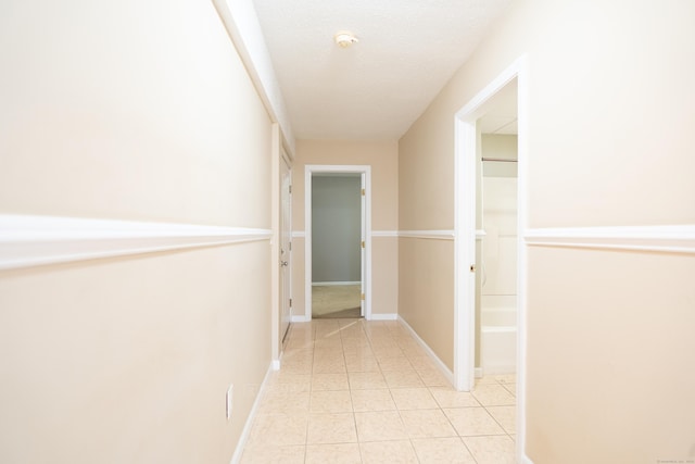 hallway featuring light tile patterned floors, a textured ceiling, and baseboards