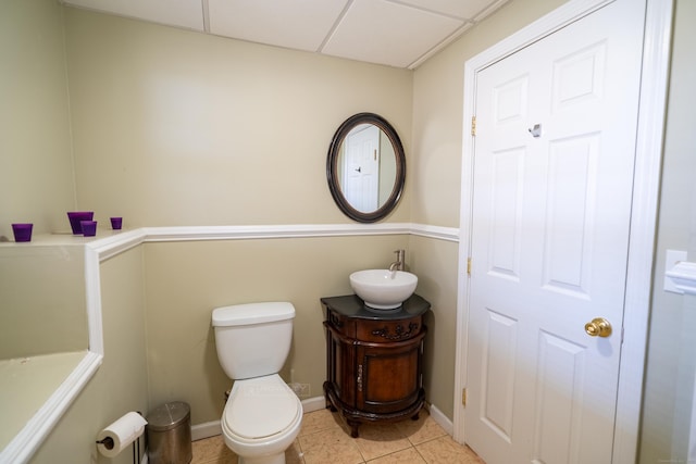 bathroom with tile patterned flooring, baseboards, toilet, vanity, and a paneled ceiling