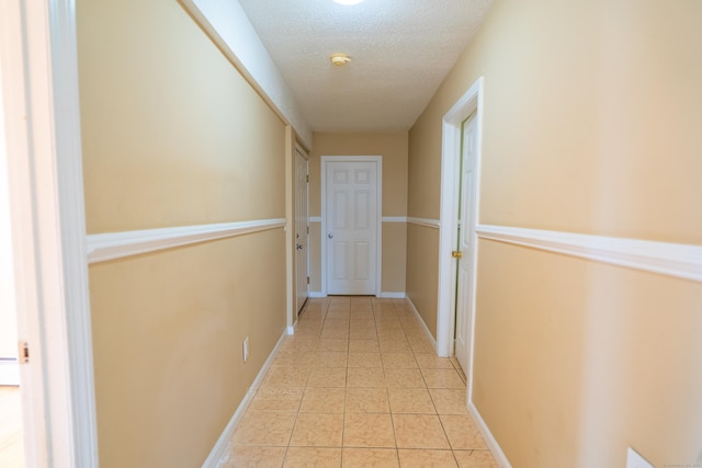 corridor featuring light tile patterned floors, baseboards, and a textured ceiling