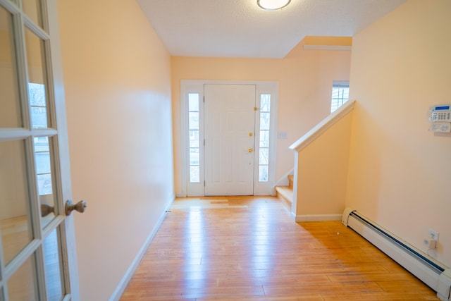 entryway with baseboards, stairs, baseboard heating, light wood-style floors, and a textured ceiling