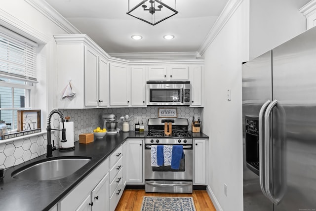 kitchen with dark countertops, appliances with stainless steel finishes, light wood-style floors, white cabinetry, and a sink