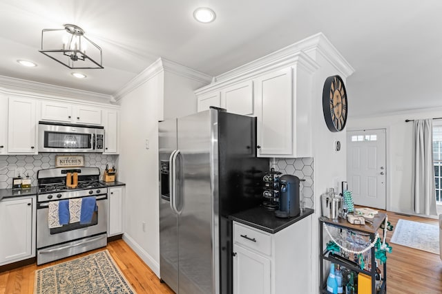 kitchen with light wood finished floors, dark countertops, ornamental molding, stainless steel appliances, and white cabinetry