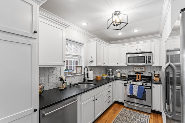 kitchen featuring white cabinets, dark countertops, stainless steel appliances, light wood-style floors, and a sink