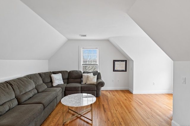 living area featuring light wood-style floors, visible vents, vaulted ceiling, and baseboards