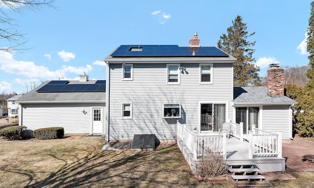 back of property featuring roof mounted solar panels, a yard, a chimney, and a wooden deck