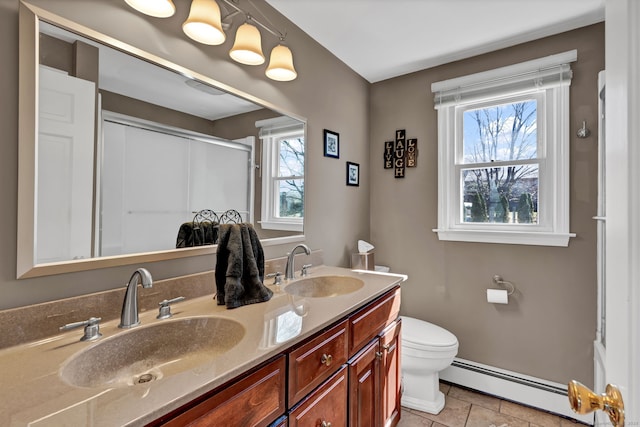 bathroom featuring double vanity, baseboard heating, a sink, and toilet