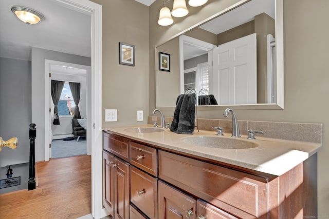 full bathroom featuring a baseboard heating unit, double vanity, a sink, and wood finished floors