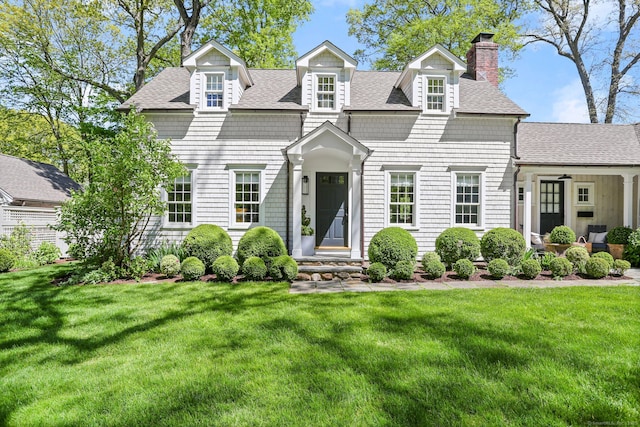 cape cod home with a shingled roof, a chimney, and a front yard