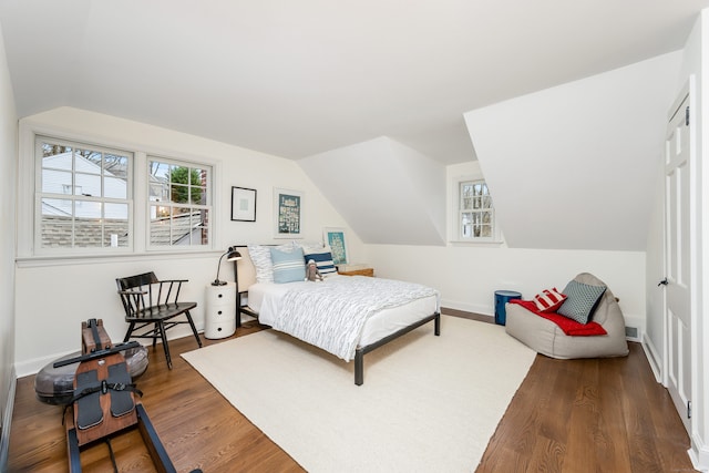 bedroom featuring lofted ceiling, multiple windows, wood finished floors, and baseboards