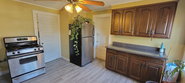 kitchen with a ceiling fan, dark countertops, appliances with stainless steel finishes, ornamental molding, and light wood-style floors