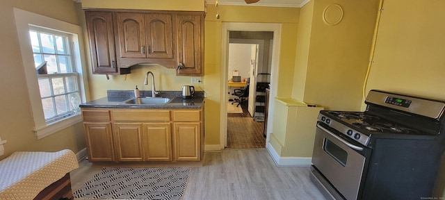 kitchen featuring light wood finished floors, baseboards, dark countertops, a sink, and gas stove