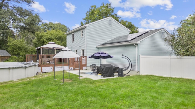 back of property featuring a covered pool, a gazebo, fence, a yard, and roof mounted solar panels