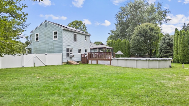 rear view of house featuring a lawn, a covered pool, a gate, fence, and a gazebo