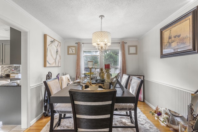 dining room with a wainscoted wall, crown molding, light wood-style flooring, a textured ceiling, and a chandelier