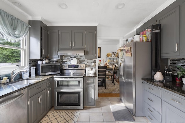 kitchen with decorative backsplash, appliances with stainless steel finishes, a sink, dark stone counters, and wall chimney exhaust hood