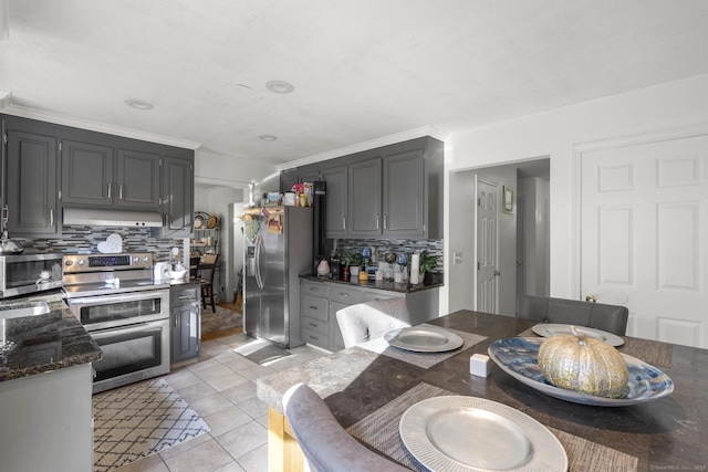 kitchen featuring light tile patterned flooring, under cabinet range hood, stainless steel appliances, backsplash, and dark stone counters