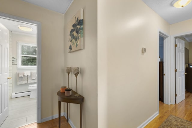 hallway featuring a baseboard heating unit, light wood-type flooring, and baseboards