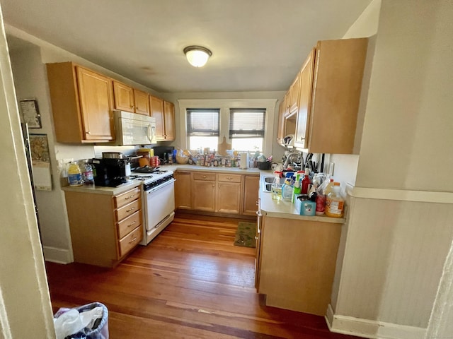 kitchen with wood finished floors, light countertops, white appliances, and a sink