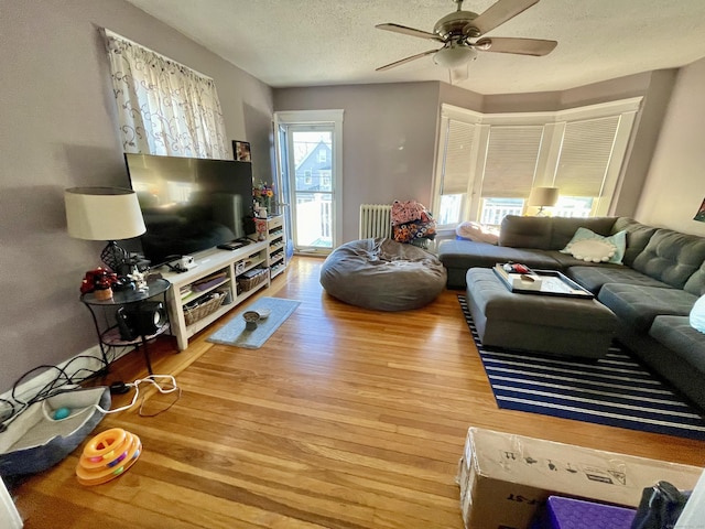 living room featuring a textured ceiling, radiator heating unit, light wood-type flooring, and a ceiling fan