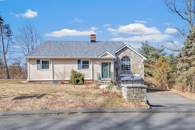 ranch-style house featuring stone siding, a chimney, driveway, and roof with shingles