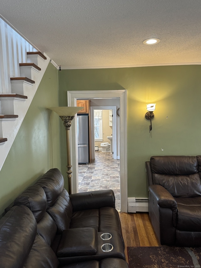 living area with a baseboard radiator, ornamental molding, a textured ceiling, wood finished floors, and stairs