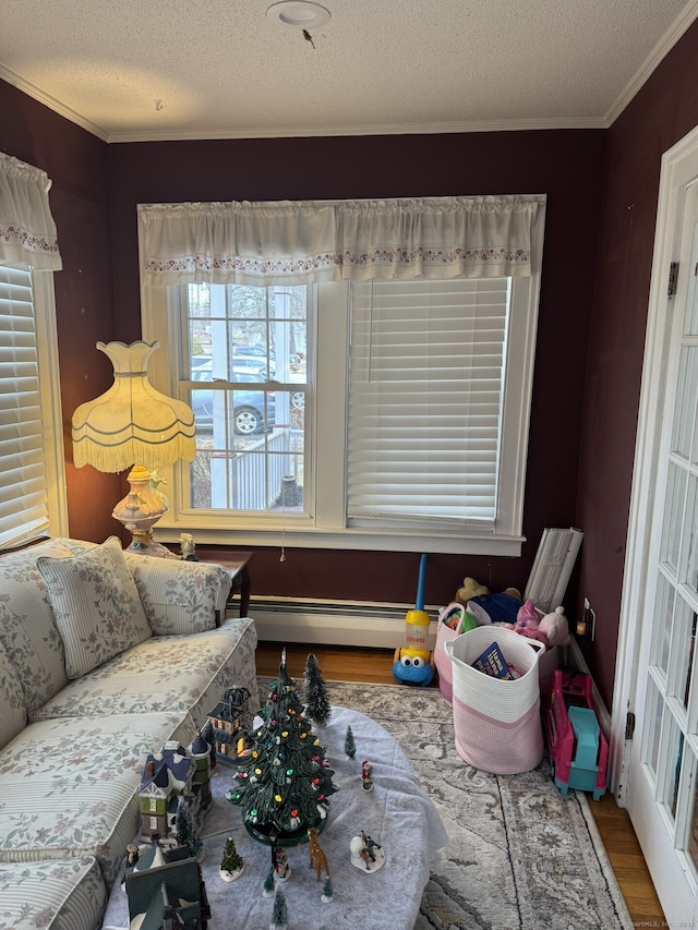 recreation room featuring a textured ceiling, ornamental molding, baseboard heating, and wood finished floors