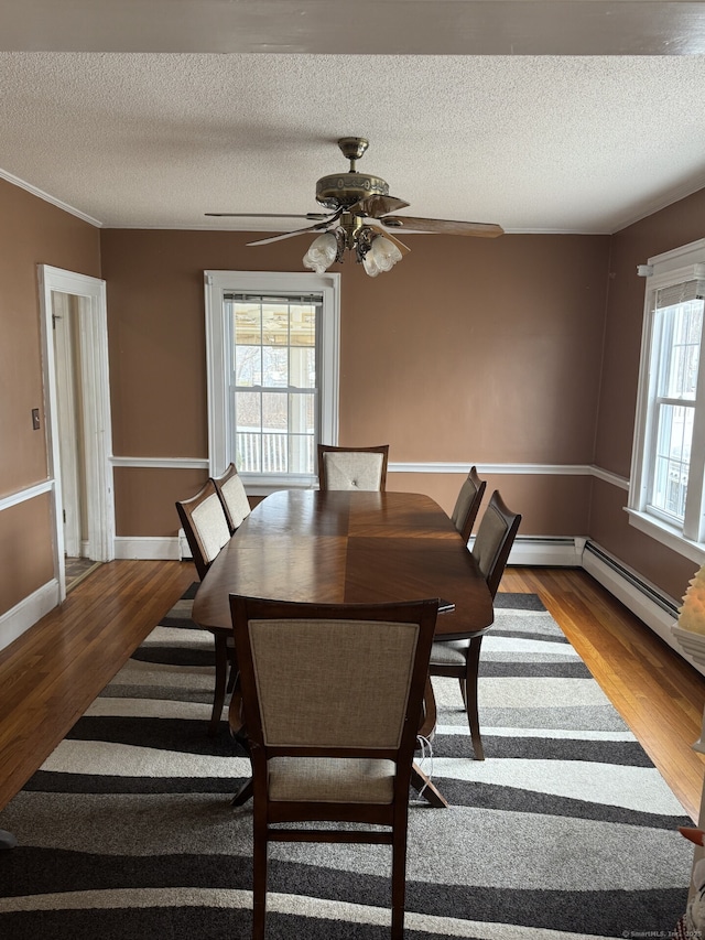 dining space with ceiling fan, a textured ceiling, baseboards, and wood finished floors