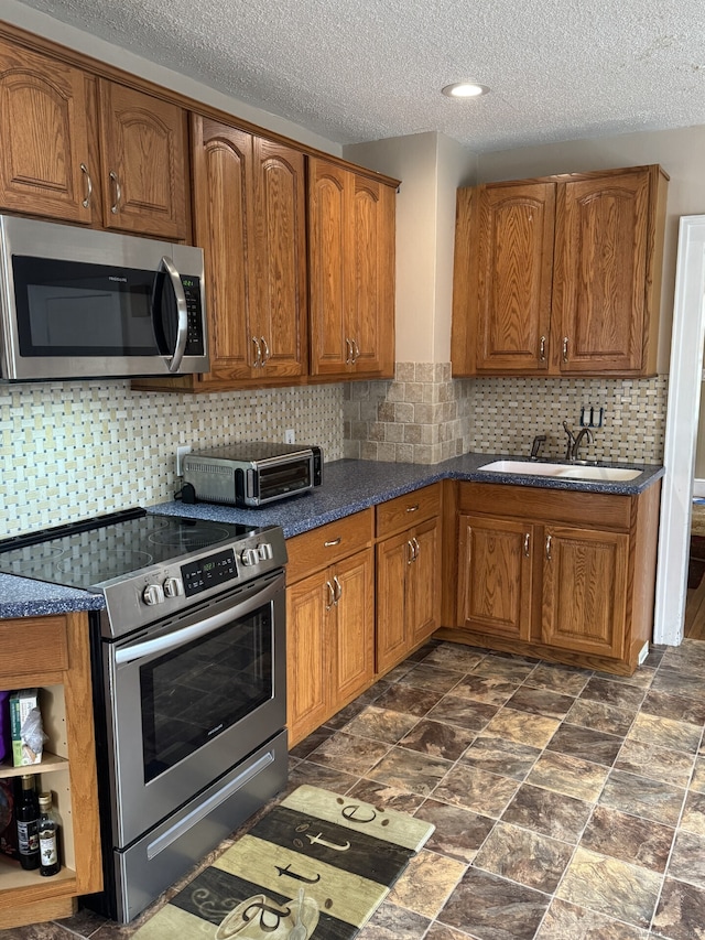 kitchen with a toaster, a sink, appliances with stainless steel finishes, brown cabinetry, and dark countertops