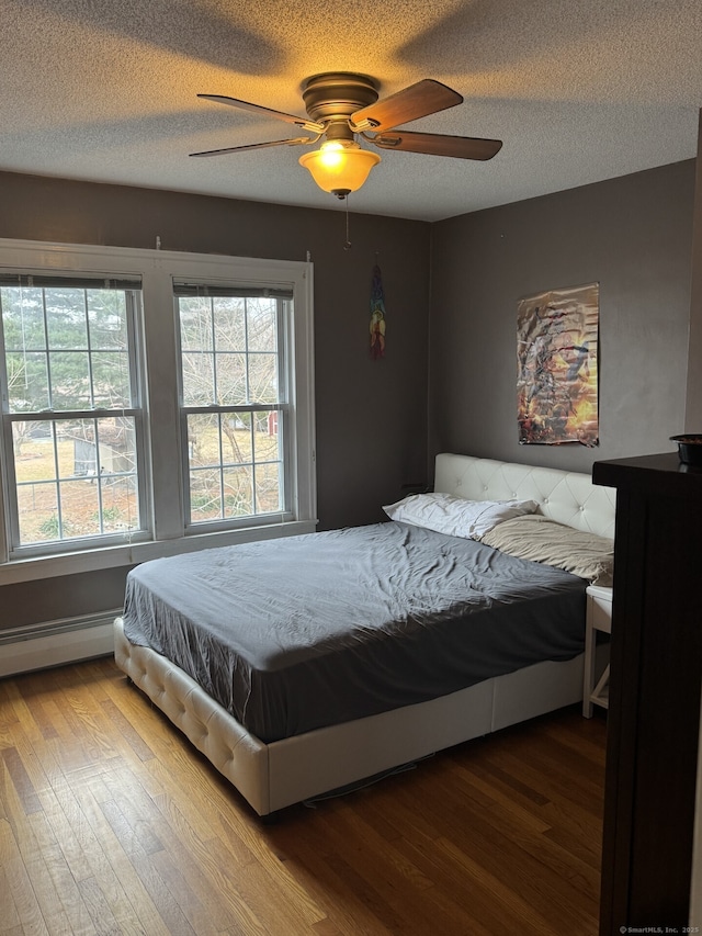 bedroom featuring a textured ceiling, multiple windows, a baseboard radiator, and wood finished floors