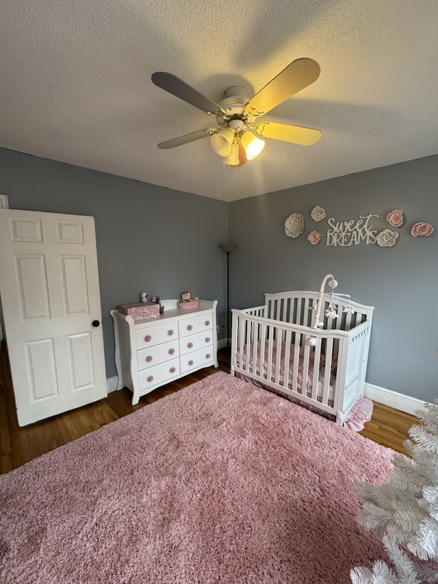 unfurnished bedroom featuring a textured ceiling, wood finished floors, a ceiling fan, baseboards, and a nursery area