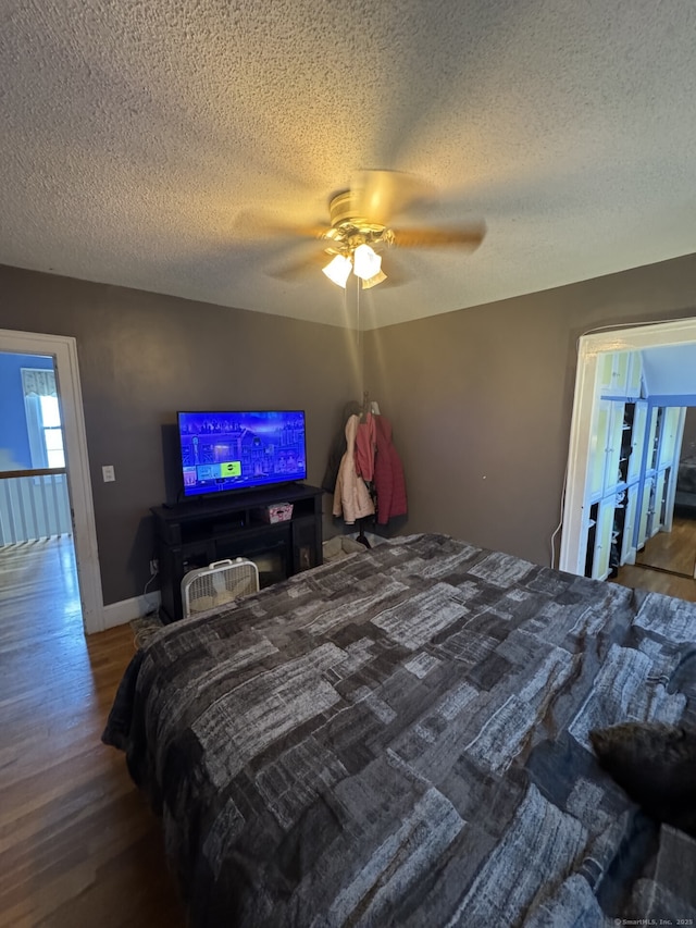 bedroom featuring ceiling fan, a textured ceiling, wood finished floors, and baseboards