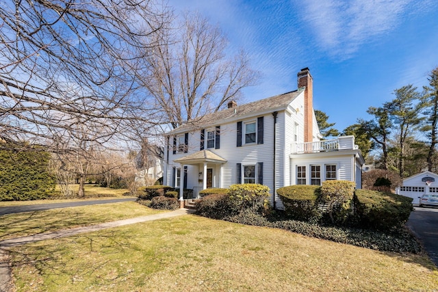 colonial home featuring a front yard, a balcony, and a chimney