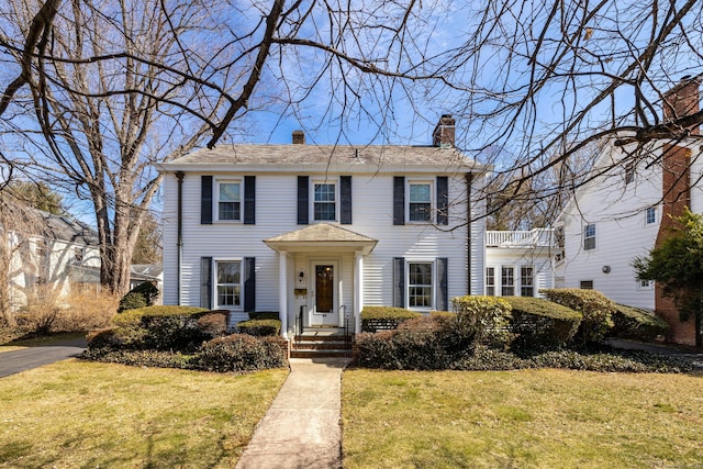 colonial inspired home featuring a balcony, a chimney, and a front lawn