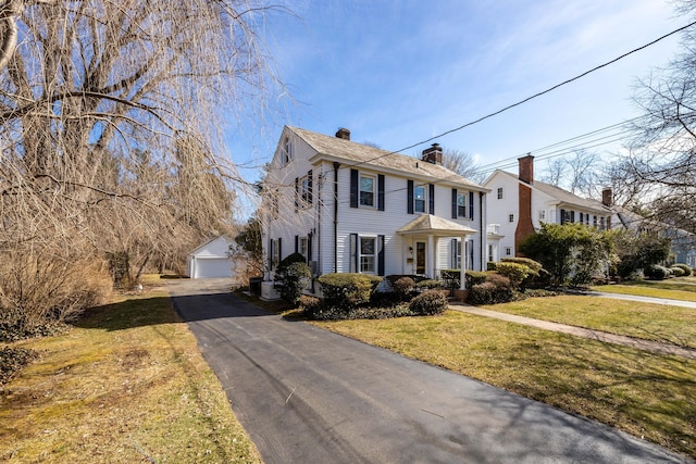 colonial inspired home with an outbuilding, a chimney, a front yard, and a garage