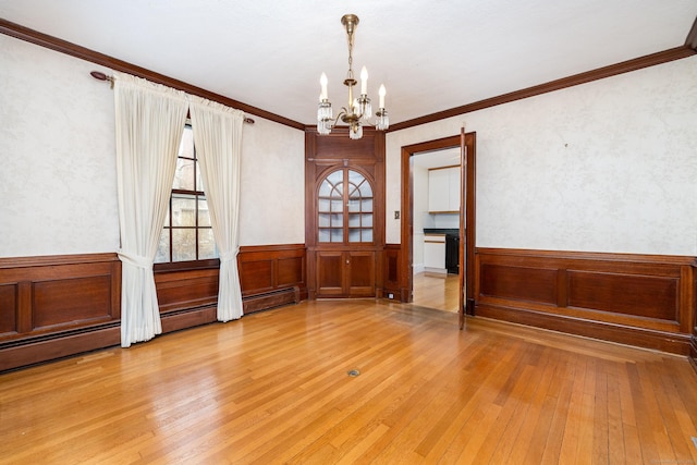 empty room featuring a wainscoted wall, light wood-style floors, and a chandelier