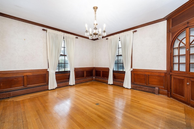 unfurnished room featuring light wood finished floors, wainscoting, an inviting chandelier, and ornamental molding