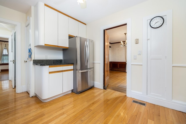 kitchen with dark countertops, visible vents, light wood-type flooring, freestanding refrigerator, and white cabinetry