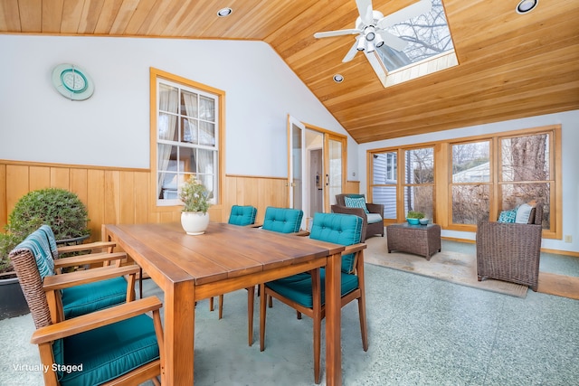 carpeted dining space featuring lofted ceiling with skylight, a ceiling fan, recessed lighting, wainscoting, and wood ceiling