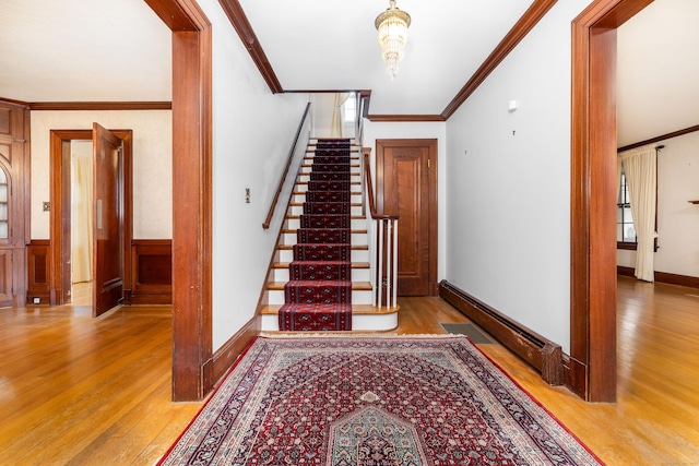 staircase with baseboard heating, wood finished floors, and crown molding