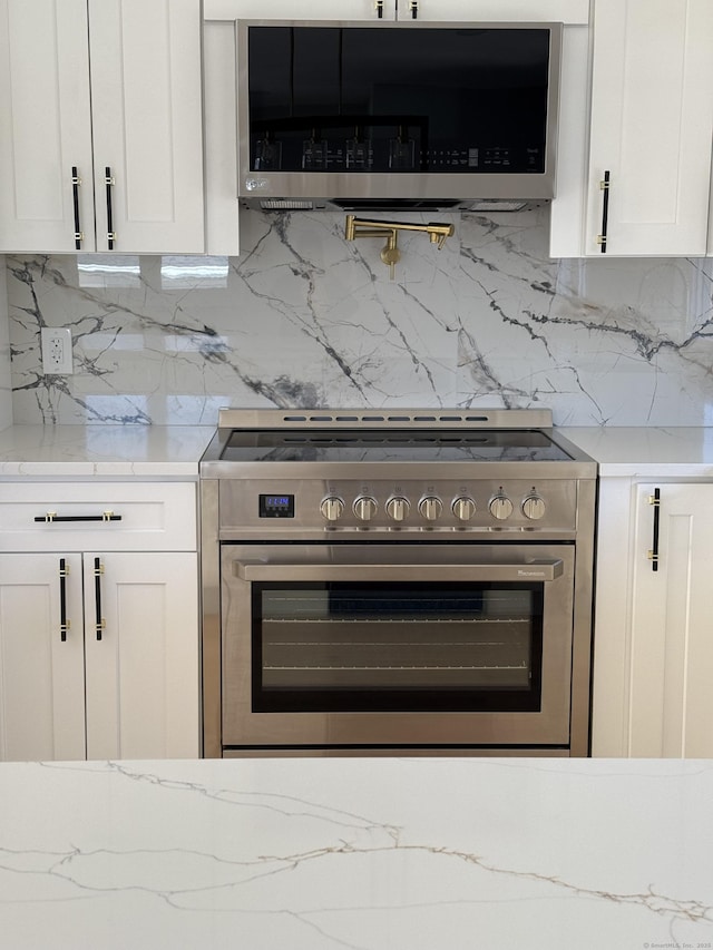 kitchen featuring appliances with stainless steel finishes, white cabinetry, light stone counters, and tasteful backsplash