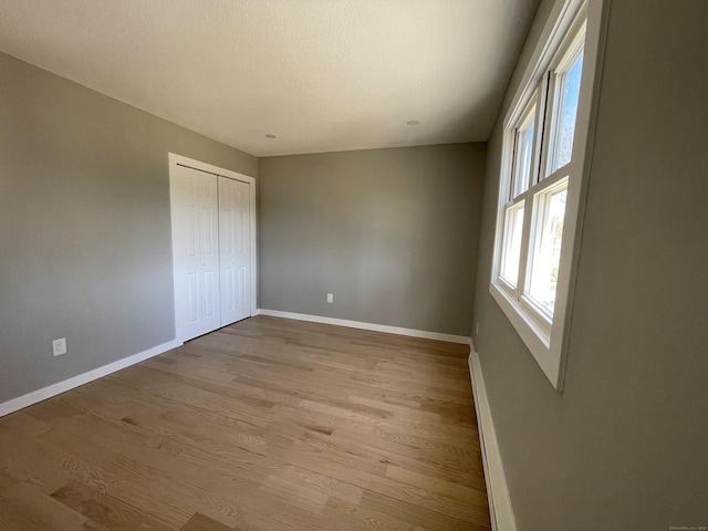 unfurnished bedroom featuring light wood finished floors, a closet, a baseboard radiator, and baseboards