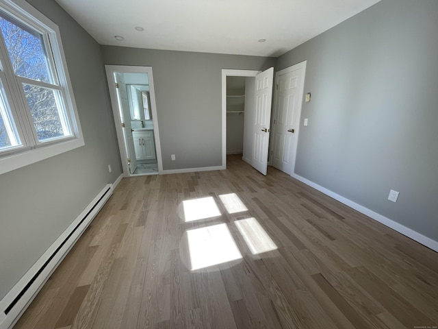 unfurnished bedroom with a baseboard radiator, a spacious closet, baseboards, and wood finished floors