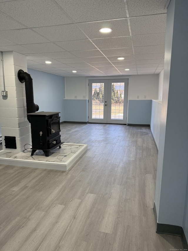 living area with french doors, a wood stove, wood finished floors, a drop ceiling, and baseboards